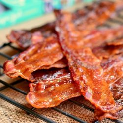 close up view of cooked bacon stacked on a cooling rack with a recipe book in background to the left