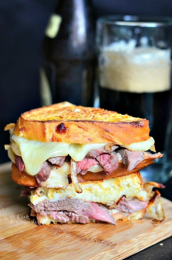 Steak and Onion Grilled Cheese cut in half and stacked on top of one another on a wood cutting board 