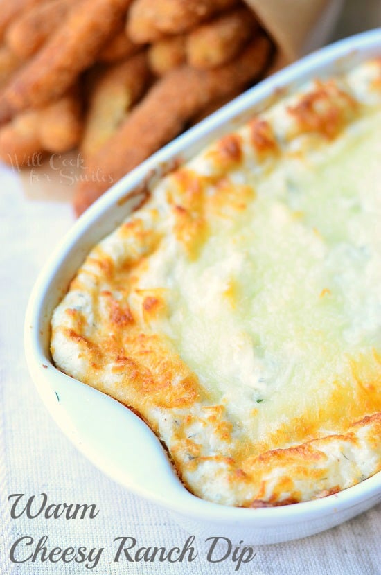 oval baking dish filled with warm cheesy ranch dip and a portion of chicken fries in the back on a white cloth