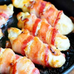 4 bacon wrapped chicken strips in a hot skillet on pot holding on wood table