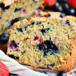 Berry Bread sliced on a wood table with strawberries and blueberries