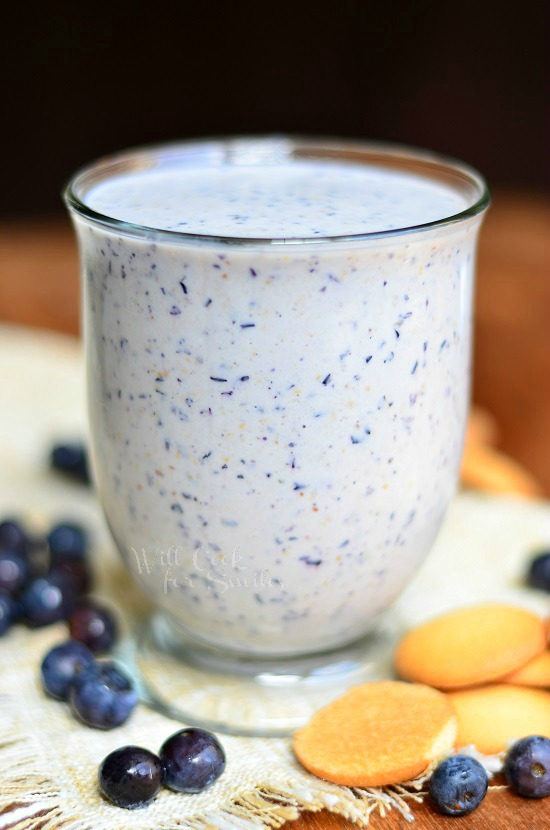 Blueberry Muffin Milkshake in a glass with blueberries and vanilla wafers around the table beside it 