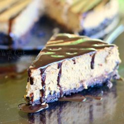 1 slice of cheesecake in front of whole cake on a black glossy table