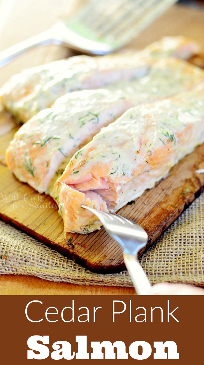 cooked Cedar Plank Salmon smothered in creamy lemon dill sauce on a cutting board with a bite on a fork and a spatula in the background 