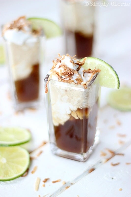 clear square shaped glass filled with dirty dr. pepper floats on a white table with lime slices to left and additional floats in background