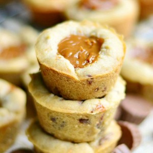 3 dulce de leche peanut butter cup cookies stacked on a brown cloth with mini peanut butter cups at bottom of stack with additional cookies in background