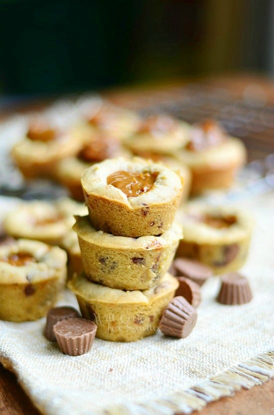 3 dulce de leche peanut butter cup cookies stacked on a brown cloth with mini peanut butter cups at bottom of stack with additional cookies in background