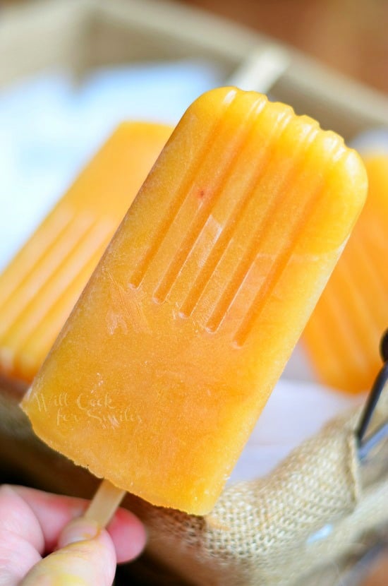 holding a orange colored Ginger Peach Green Tea Popsicle