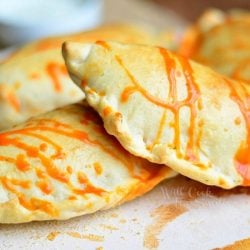 4 homemade buffalo chicken calzoneson a white plate with buffalo sauce drizzled across top