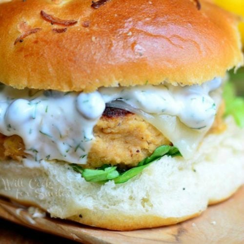 labeled Salmon burger on a bun on wood plank with white sauce on patty.