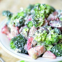 close up view of white bowl filled with strawberry broccoli salad on a white and green cloth with fork to the left