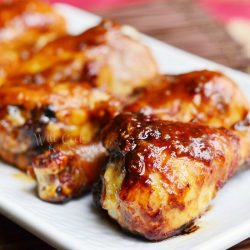 close up view of 5 asian roasted drumsticks on a rectangular white plate resting on a bamboo placemat