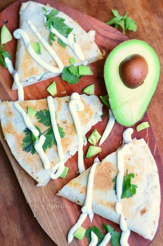 Avocado Chicken Quesadilla on a cutting board with cilantro and sliced avocado on top and half an avocado on the top 