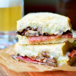 cut and stacked bourbon bacon mushroom abd onion grilled cheese on a brown wax paper wrapper on wood cutting board with a glass beer mug in the background filled halfway with beer