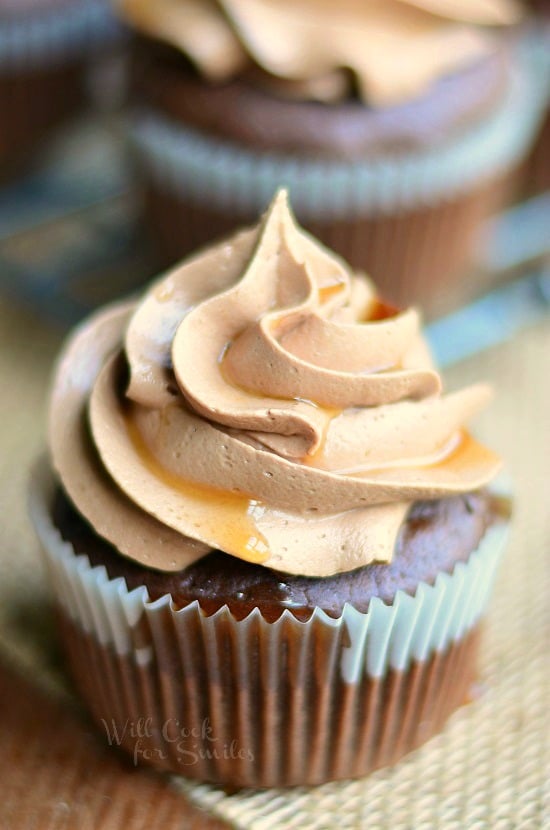 1 bourbon cupcake in cupcake wrapper on brown placemat on wood table with additional cupcakes in background