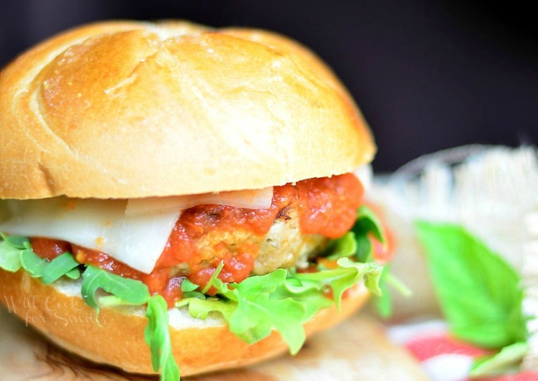 horizonal photo of Chicken Parmesan Burger with basil on the bun on a wood cutting board 