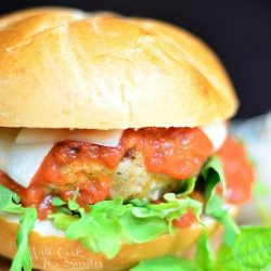 chicken parmesan burger on a wood cutting board with a red and white cloth below cutting board and a black background