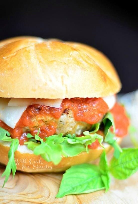 chicken parmesan burger on a wood cutting board with a red and white cloth below cutting board and a black background