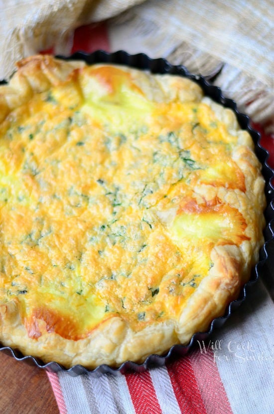 The top view of a Four Cheese Souffle still in it's baking dish. It has flaky puff pastry with some fresh herbs and cheese.