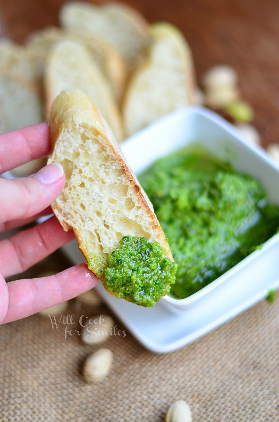 bread that has been dipped into pesto and the Lemon Pistachio Arugula Pesto in a small white square bowl 