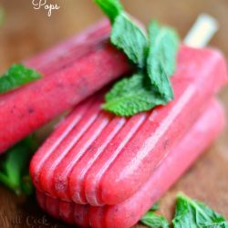 3 strawberry mojito pops on a wooden table with mint leaves dressed across pops