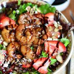 shrimp salad with balsamic reduction dressing on a tan cloth on wood table with small white bowl with more reduction and small spoon in background