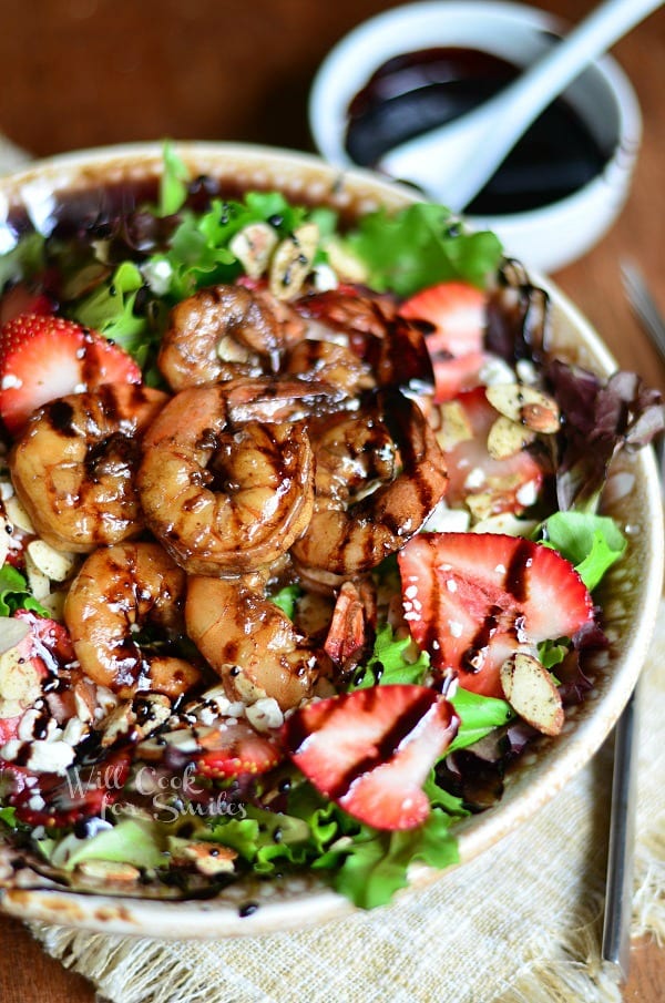 Balsamic Shrimp Salad is shown served in a bowl. Lots of greens in this salad that are topped with fresh strawberries, shrimp, and a balsamic reduction.