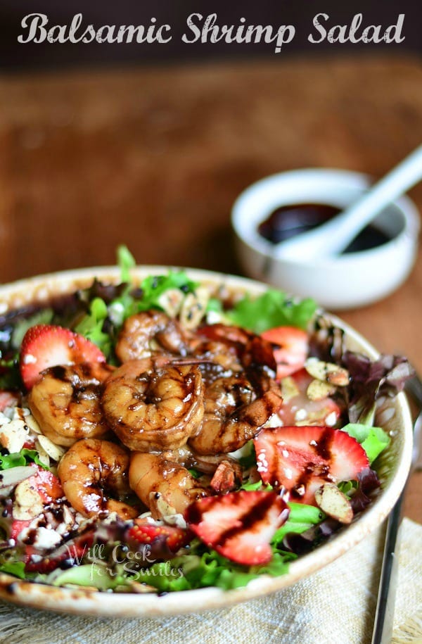 Balsamic Shrimp Salad on a brown plate with shrimp and strawberries and a bowl of dressing at the top right