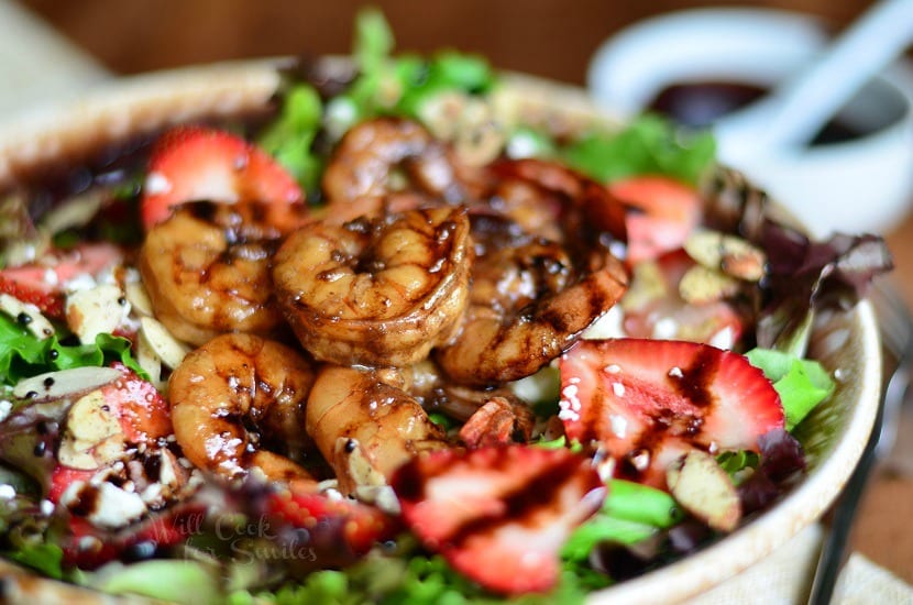 Horizonal photo Balsamic Shrimp Salad on a brown plate with shrimp and strawberries and a bowl of dressing at the top right