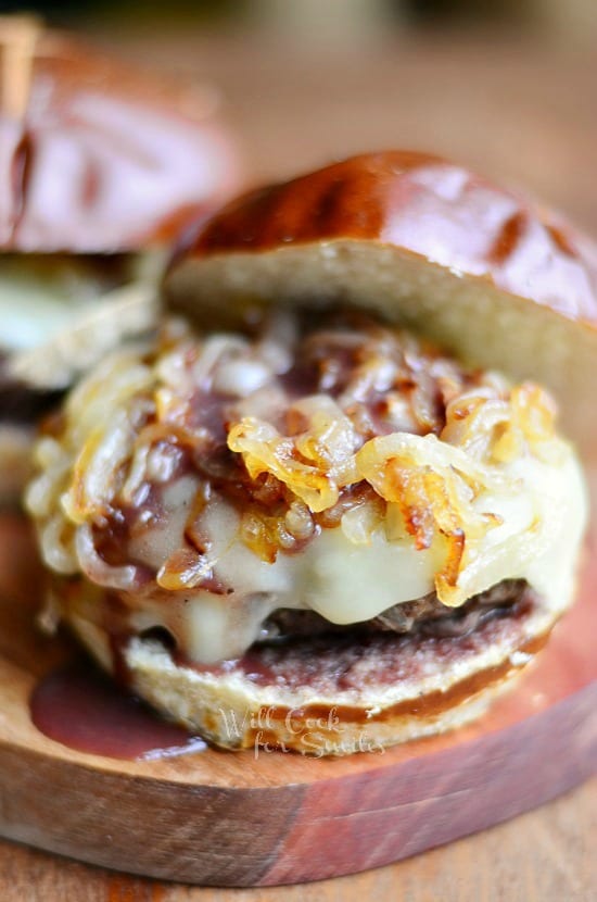 2 buffalo burgers with caramelized onions and demi glace sauce on a wood cutting board