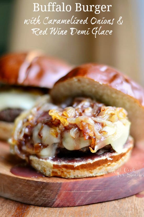 Buffalo Burger on a bun with Caramelized Onions and Red Wine Demi Glace on top on a wood cutting board 