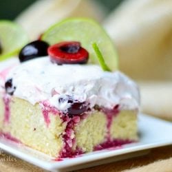 1 slice of cherry limeade poke cake on white rectangular plate in foregroundon a brown placemat with additional slices in background