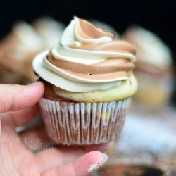 hand holding 1 marble cupcake with marble cream cheese frosting with additional cupcakes in background
