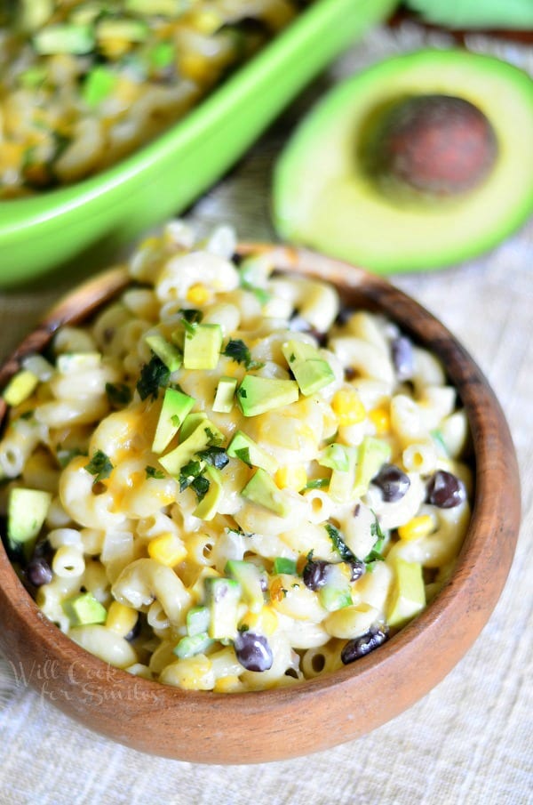 Tex-Mex Mac and Cheese in a wood bowl with an avocado to the top right 