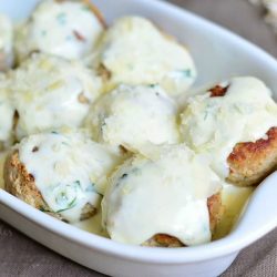close up view of small ovalwhite baking dish filled with turkey meatballs with creamy parmesan sauce on a grey cloth