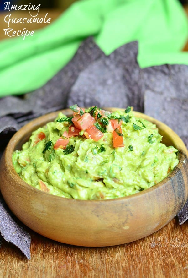 Amazing Guacamole in a wood bowl with purple tortilla chips around it on a wood table 