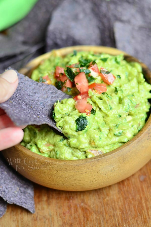 scooping some guacamole with a blue corn tortilla chip