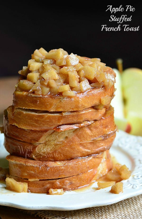 Stacked Apple Pie Stuffed French Toast served on a white plate. The top is loaded with apples and syrup, which runs down onto the plate.