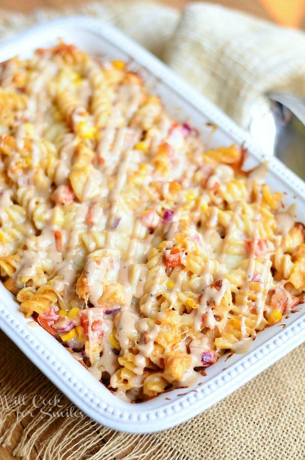 BBQ Ranch Chicken Casserole served in a white casserole dish. Pasta is drizzled with a BBQ ranch sauce.