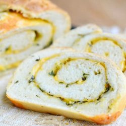 close up view of 2 slices of cheddar herb swirl bread on a brown placemat with the rest of the loaf behind in background