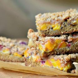 3 peach crumble cookie bars stacked on a brown piece of wax paper on a wooden table