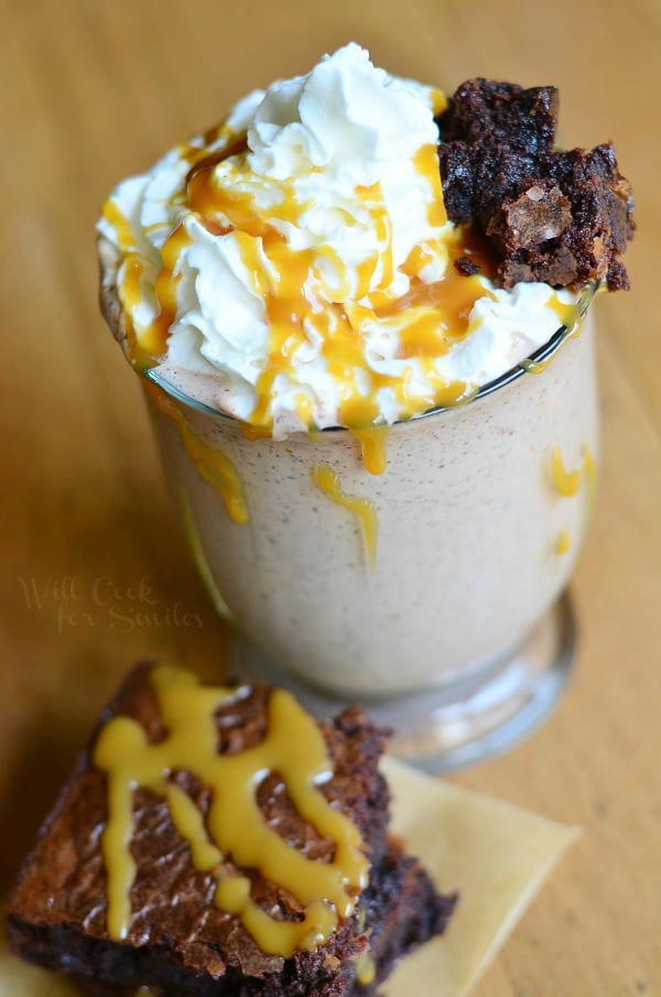 Salted Caramel Brownie Milkshake in a glass with whipped cream, caramel on top with a brownie on top and to the side of the glass 