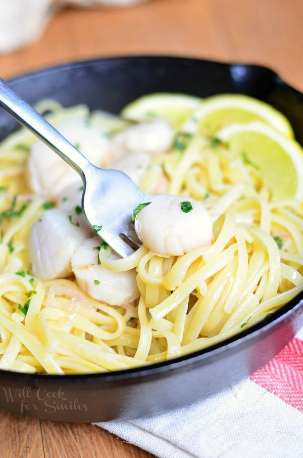 Scallop Scampi in a cast iron skillet with a fork picking scooping some up 