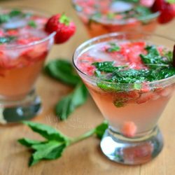 close up of 3 short stem martini glasses filled with skinny strawberry mojito on a wooden table with each glass topped with a strawberry garnish and mint