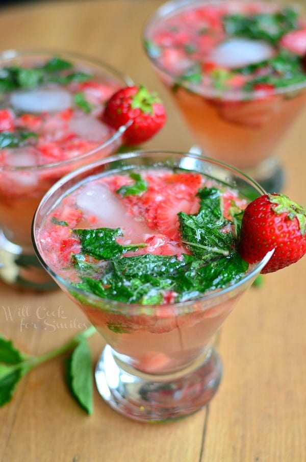 view from above and close up of 3 short stem martini glasses filled with skinny strawberry mojito on a wooden table with each glass topped with a strawberry garnish and mint