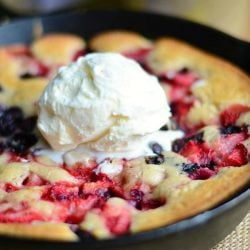 clsoe up of trile berry skillet tea cobbler topped with ice cream on a brown placemat on a wood table