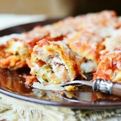 fork with portion cut of manicotti on black plate with 3 pieces in background on plate as well.