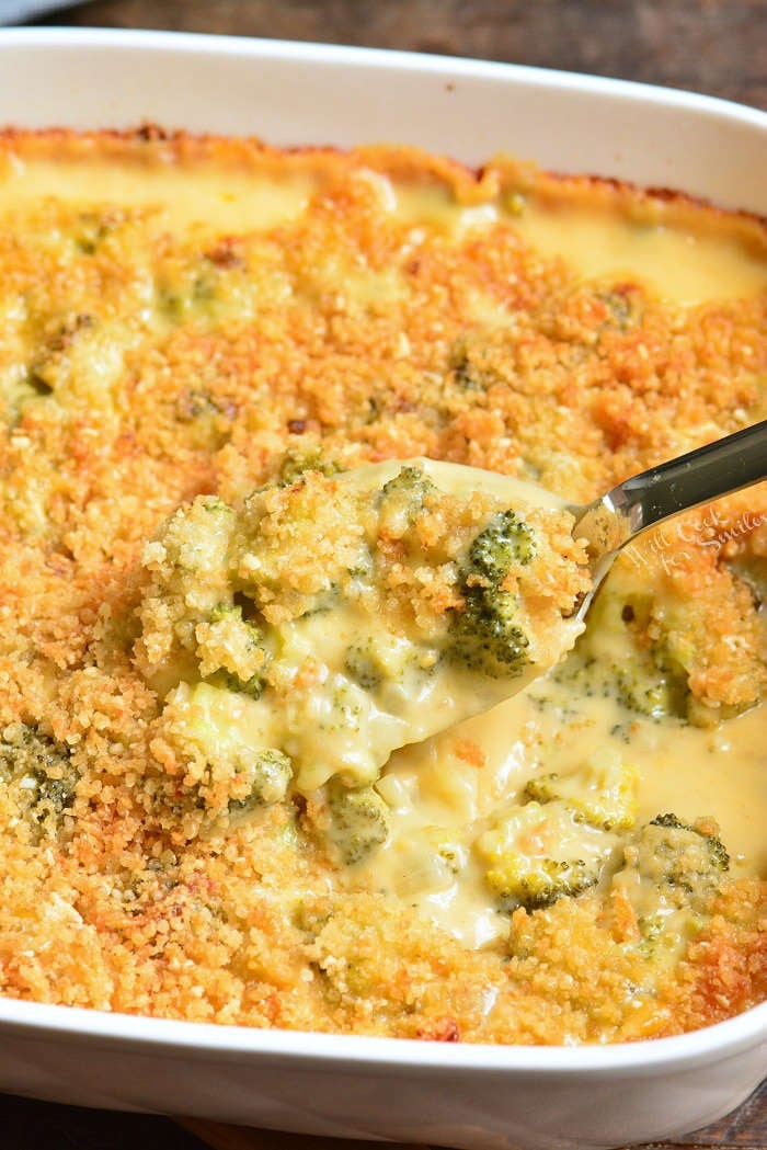 broccoli casserole in a baking dish with a serving spoon scooping it out siting on a wood table 