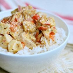 close up view of white bowl filled to the brim with creamy cajun chicken rice on a white table cloth on wooden table with another white and red cloth in background