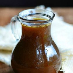 syrup jar filled with homemade pumpkin syrup on a wooden table with a white cloth in the background